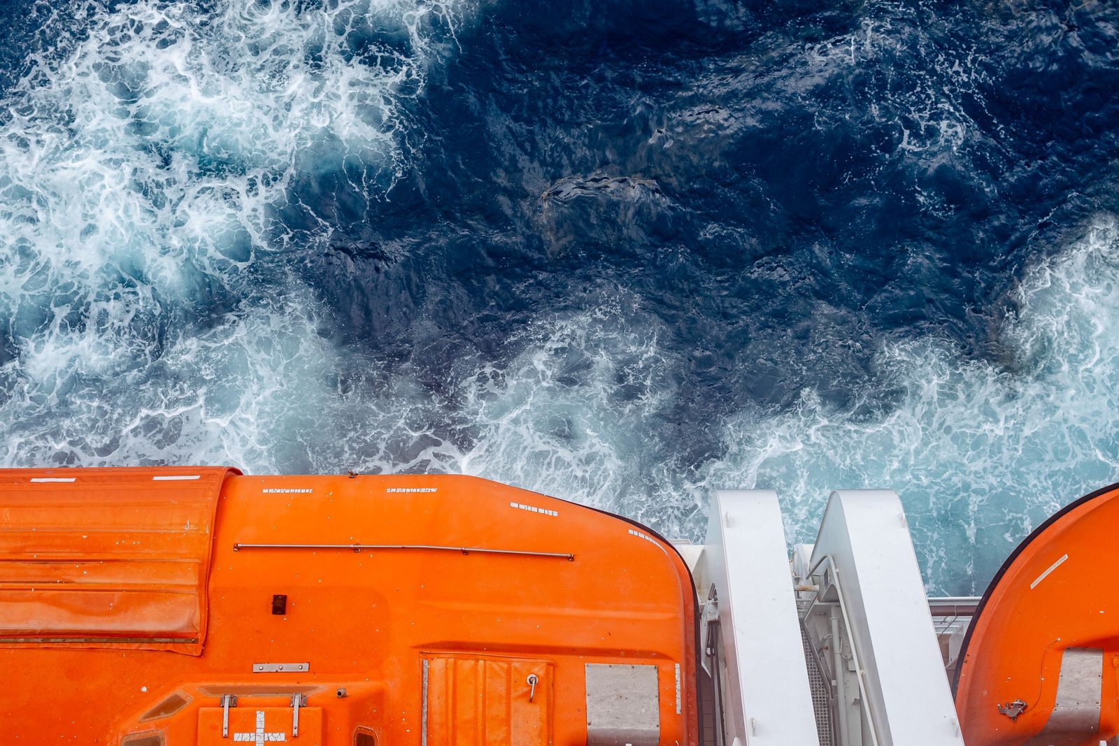 Orange lifeboats above a ship&rsquo;s white wake, a reminder that travel industry cruise discounts come with rules